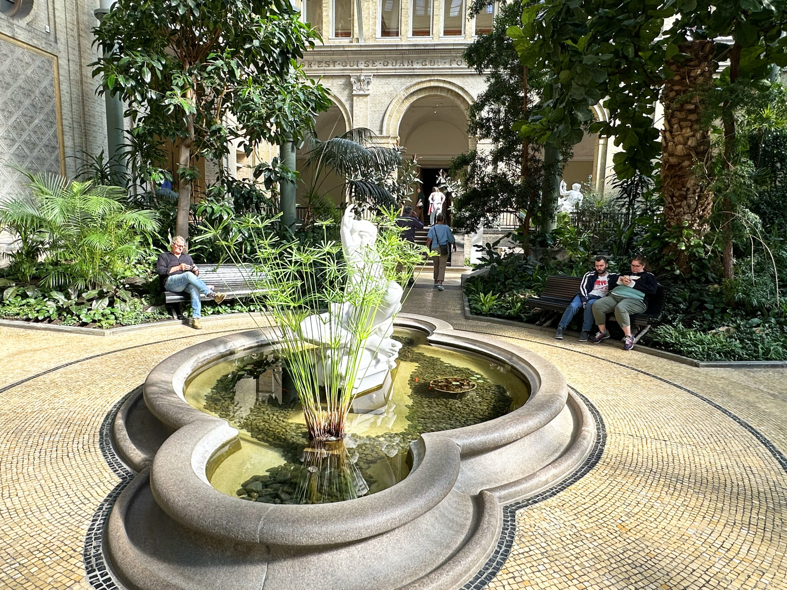 Personer som sitter vid fontän på museet Glyptoteket i Köpenhamn.