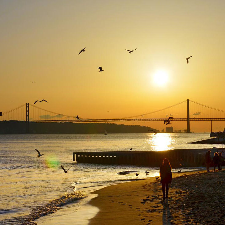 Kvinna promenerar på strand i Lissabon under solnedgång