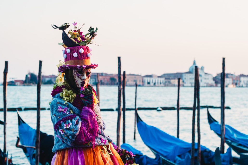 Kvinna i kostym och mask framför gondoler i Venedig under karnevalen.