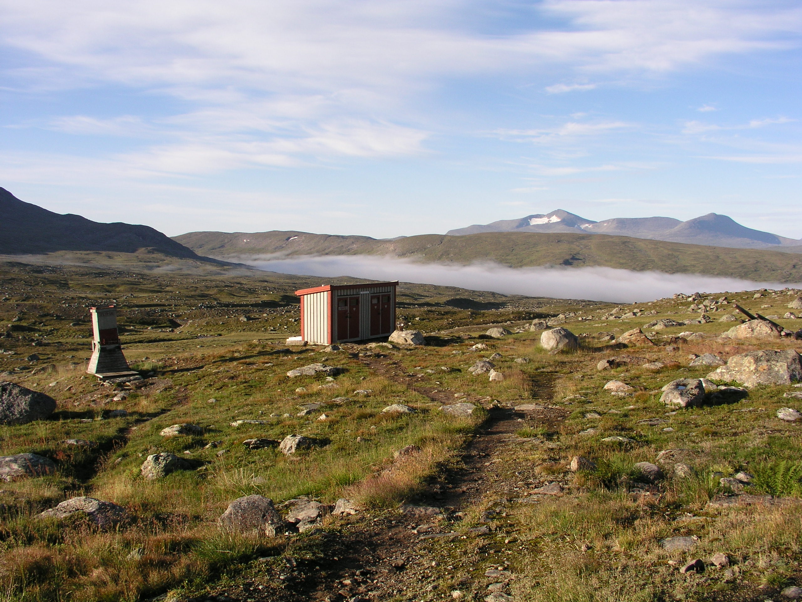 Stuga vid vandringsled, dimma som ligger över landskap, berg i bakgrund. Sommar i svenska fjällen.