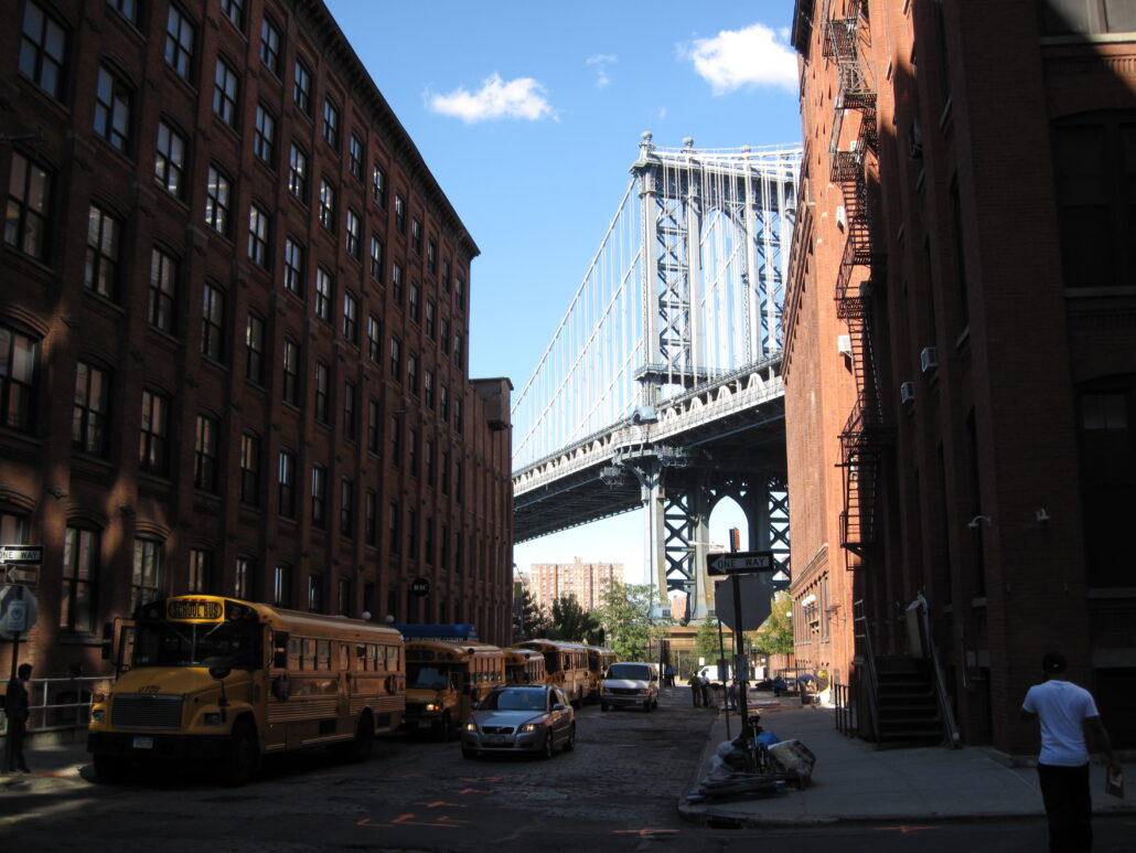 Skolbuss och trafik på gata vid byggnader vid Brooklyn Bridge i New York.