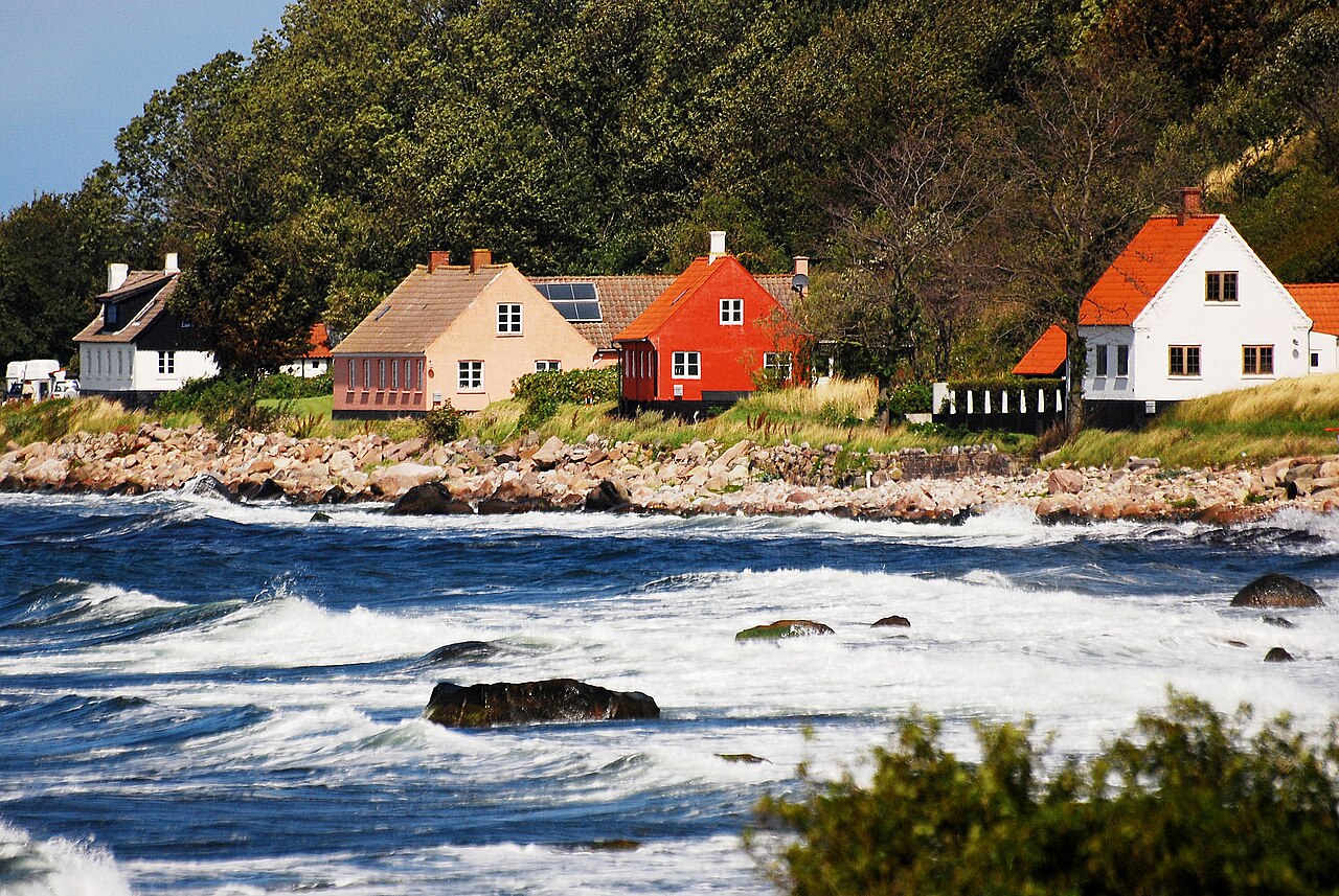 Vågor i havet vid Bornholm, hus vid hamnen, en kulle bakom.