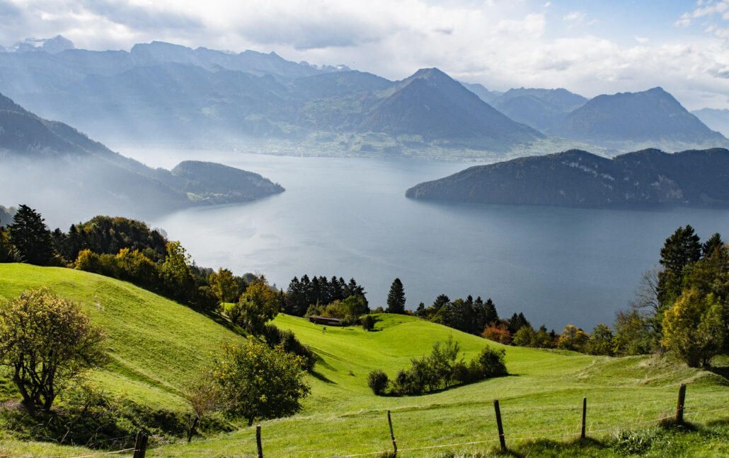 Lugensjön i Schweiz, ängar och landskap i förgrunden, bergskedja i bakgrunden. Sommar.